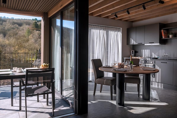 Una cocina moderna con zona de comedor, ventanas amplias y vistas a un área boscosa.