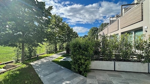 A modern outdoor area with a paved walkway, green grass, and trees. - Deluxe apartment the Chestnut (Madonna della Castagna)