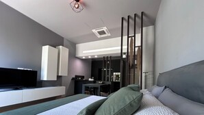 A modern bedroom with a large bed, a flat-screen TV, and a kitchenette in the background. - Deluxe apartment the Chestnut (Madonna della Castagna)