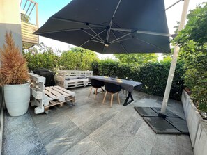 A patio with a table and chairs under a large umbrella, surrounded by potted plants and wooden pallets. - Deluxe apartment the Chestnut (Madonna della Castagna)