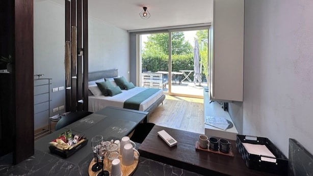 A modern hotel room with a bed, a desk with a laptop, a coffee table with drinks, and a view of the outdoors. - Deluxe apartment the Chestnut (Madonna della Castagna)