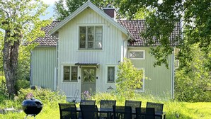 Ett tvåvåningshus med en veranda på framsidan, en grill och ett bord med stolar på gården.