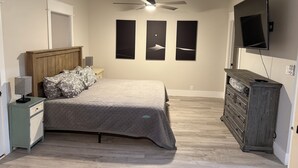 Un dormitorio con cama, mesitas de noche, cómoda, ventilador de techo y tres marcos de cuadros en la pared.