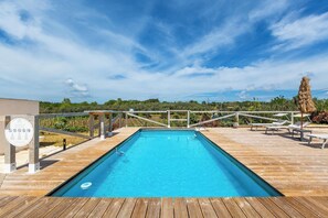 Una piscina rectangular con muelle de madera, rodeada de sillas de descanso y una valla de madera.