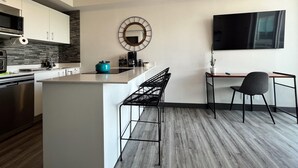 A modern kitchen with a central island, a dining area with a TV, and a workspace with a chair. - Secrt Sabana 1BR · Workspace + WiFi · Parking · Apt 1508 (Mata Redonda)