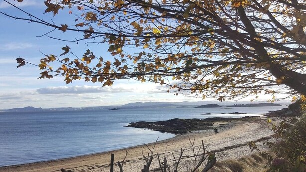 Una playa con una valla de madera, vista despejada al mar y montañas distantes.