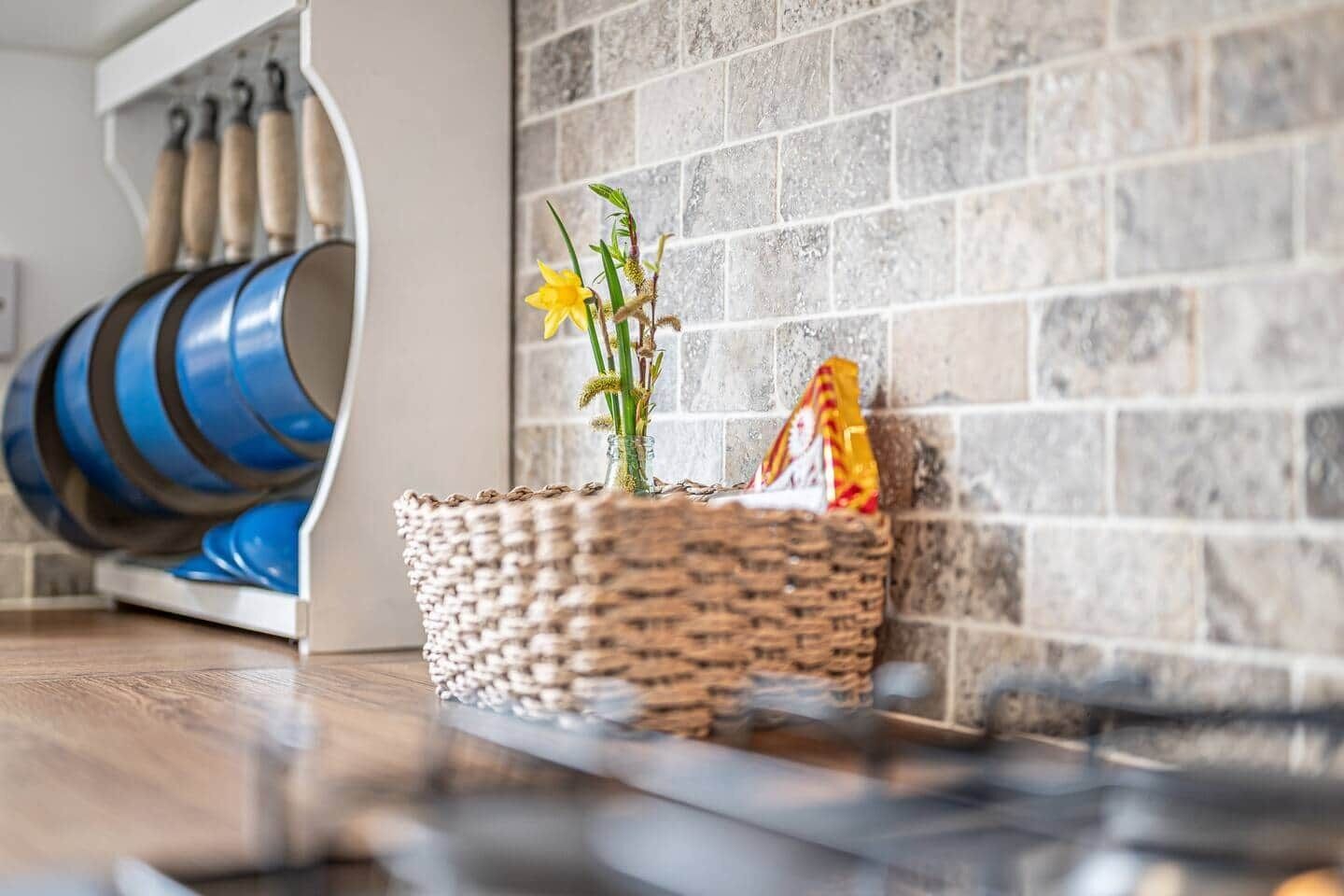Een gevlochten mand met een klein plantje en een pakje op een houten vloer, naast een stenen muur.