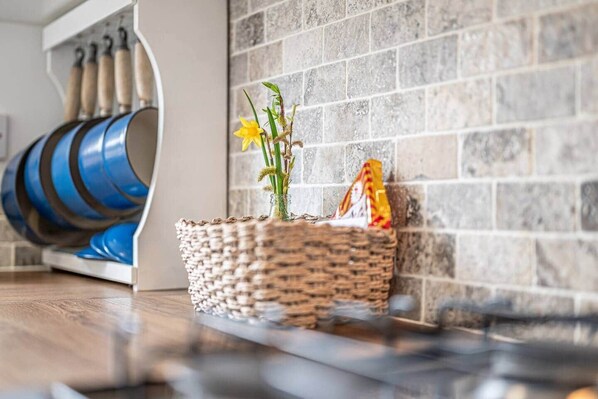 A woven basket with a small plant and a packet on a wooden floor next to a stone wall.