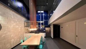 A modern kitchen with a central island, a dining area with teal chairs, and a brick wall.