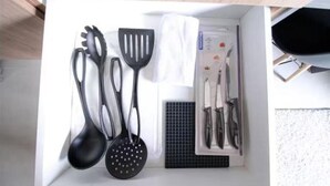 A kitchen drawer with black kitchen utensils, including a ladle, spatula, and spatula holder.