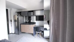 A compact, modern room with a kitchenette, a bed, and a desk.