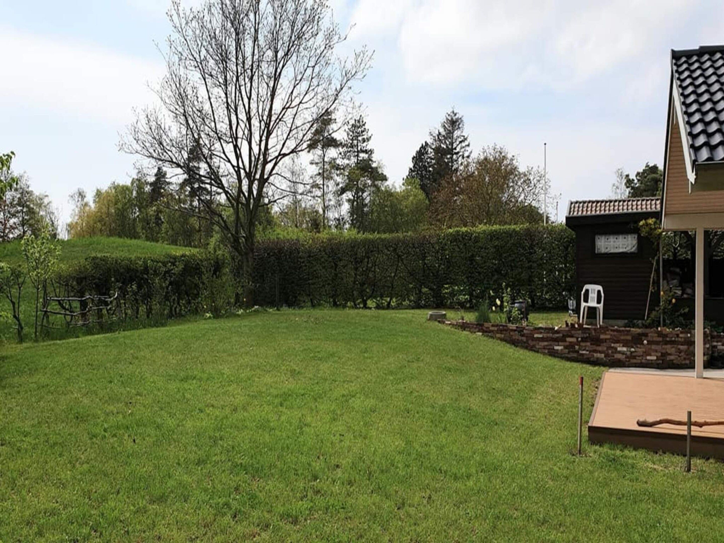 A well-maintained grassy backyard with a wooden deck, a brick planter, and a white plastic chair.