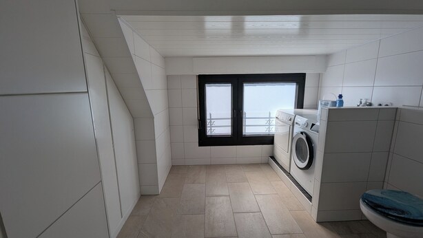 A compact laundry room with a washing machine, a window with a view, and a toilet.