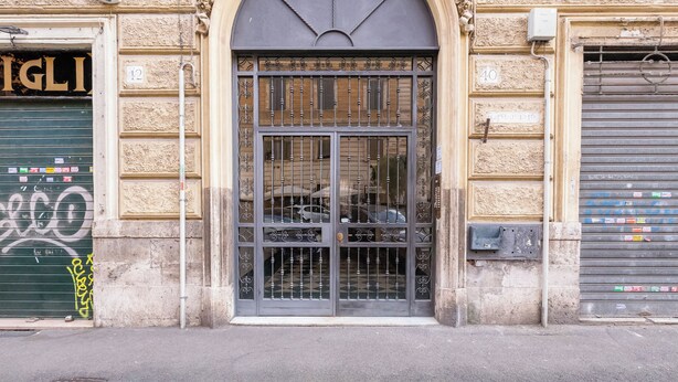A building facade with a large arched entrance, a metal gate, and a garage door with a number sign. - Recently renovated, within walking distance of the Vatican and 180mt from the metro. (Roma)