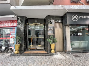 A building entrance with a black gate, a doormat, and two potted plants.