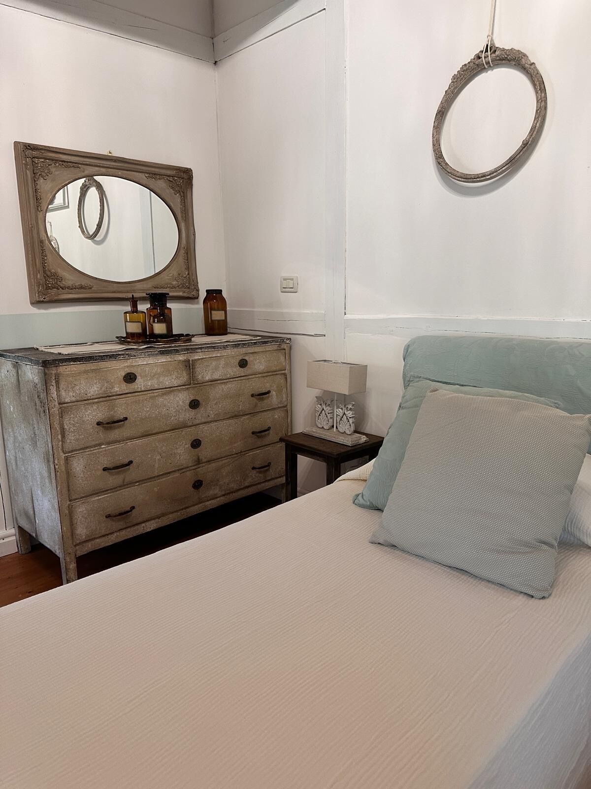 Une chambre à coucher comprenant un lit, une commode, un miroir et un anneau lumineux fixé au mur.
