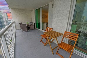 Uma varanda com mesa e cadeiras, uma porta de correr de vidro e vista para a paisagem urbana.