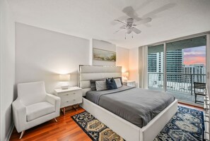 Quarto moderno com uma cama grande, uma poltrona branca, uma mesa de cabeceira e um ventilador de teto.