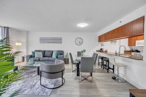 A modern living room with a grey sofa, a coffee table, and a dining area with a glass table and chairs.
