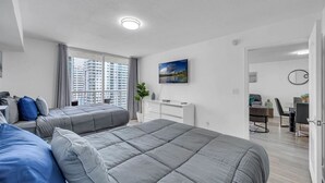 A modern bedroom with a large bed, a desk, and a view of high-rise buildings.