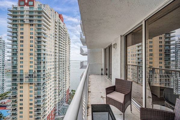 A balcony with wicker furniture, a view of high-rise buildings, and a body of water in the background. - Peaceful Brickell 1BR | Water & City Outlook (Miami)