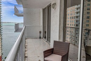 A balcony with a wicker chair, a view of the water, and a building in the background. - Peaceful Brickell 1BR | Water & City Outlook (Miami)