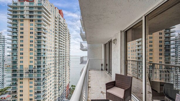 A balcony with wicker furniture, a view of high-rise buildings, and a body of water in the background.