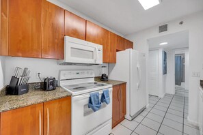 Una cocina con armarios de madera, estufa blanca, microondas y refrigerador.