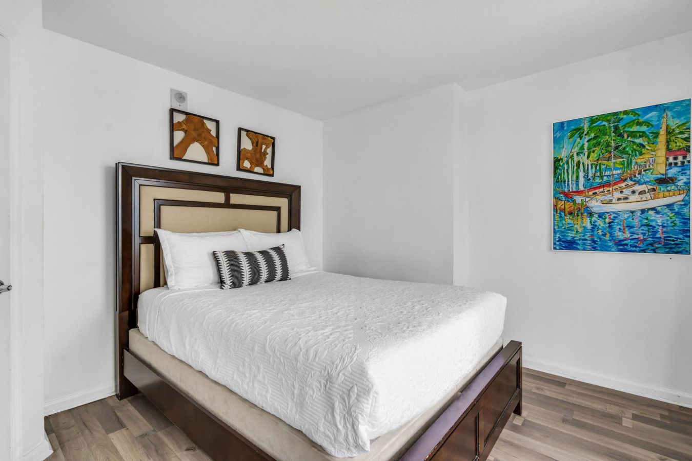 A single-bed room with a wooden headboard, white bedding, and a painting of a tropical scene.