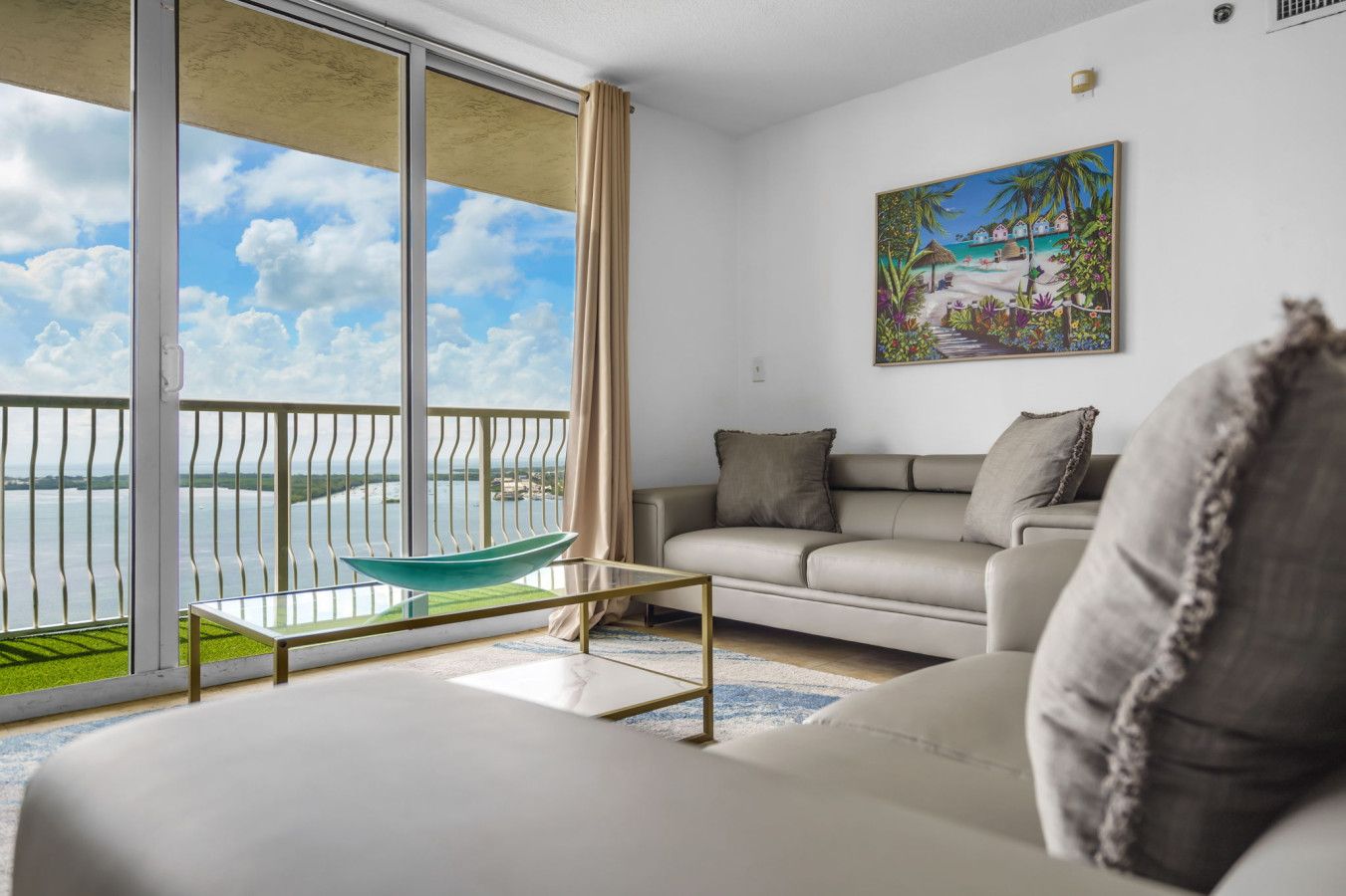 A living room with a sofa, a glass coffee table, and a painting on the wall.