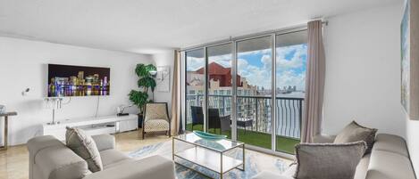 A modern living room with a large sliding glass door leading to a balcony with a city view.