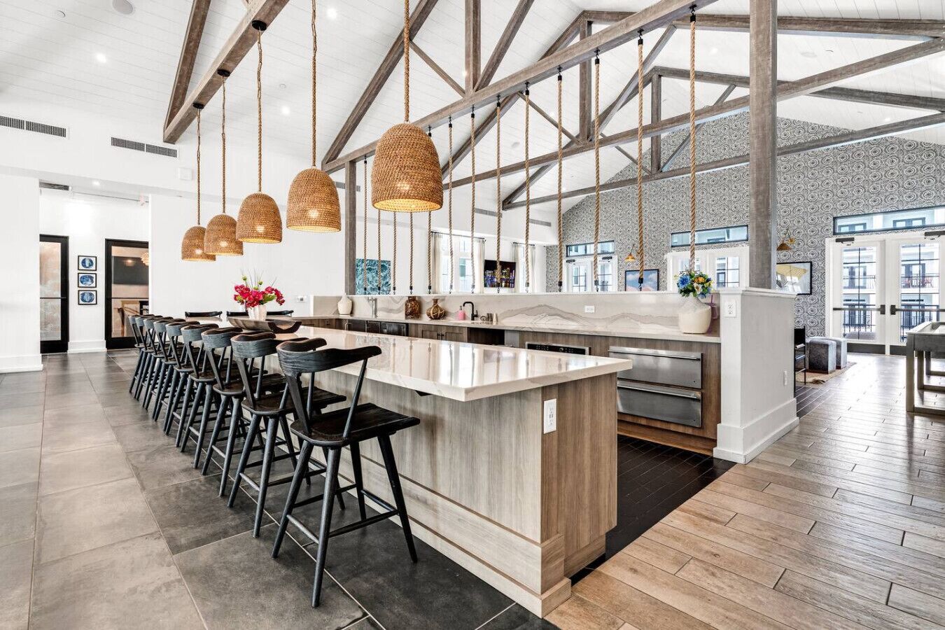A modern kitchen with a central island, bar stools, hanging wicker pendant lights, and a view of the city through large windows.