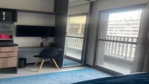 A hotel room with a bed, a desk, a chair, a TV, and a balcony with a railing.