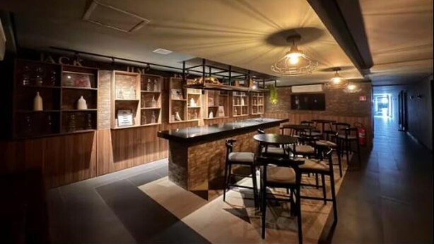 A bar area with a counter and seating. Shelves with bottles and glasses are visible.