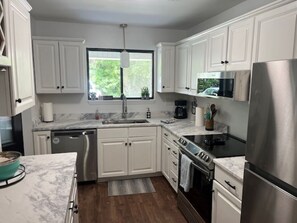 A modern kitchen with white cabinets, a stainless steel refrigerator, a microwave, and a stove.