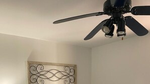 Un dormitorio con cama, una mesita de noche, un adorno en la pared y un ventilador de techo.