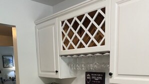 Una cocina con muebles blancos, encimera de mármol y una estantería para vinos sobre el lavabo.