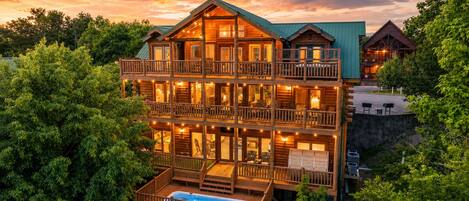 A multi-story log cabin with balconies, a pool, and a view of the surrounding forest.
