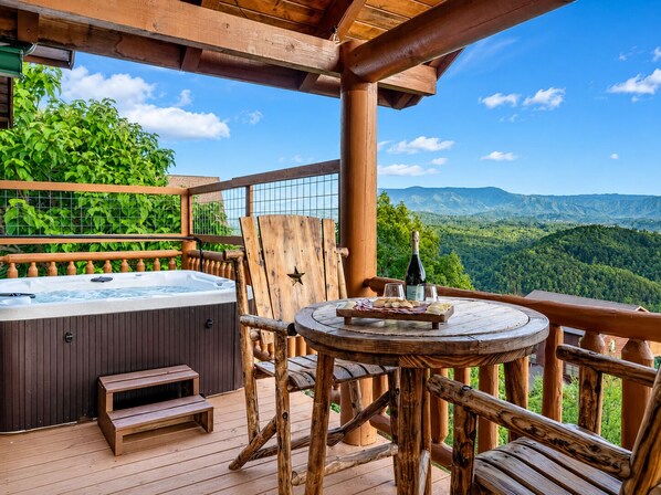 Eine Holzterrasse mit Whirlpool, einem Tisch mit Speisen und Blick auf die Berge.