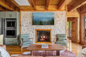 L’intérieur chaleureux d’un chalet avec une cheminée en pierre, une table à manger et un coin cuisine doté d’appareils électroménagers intégrés.