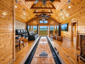 A log cabin interior with a fireplace, seating area, and a view of the mountains. - 8BR Sleeps 40 | Pool + Sauna + Hot Tub + Putt Putt (Sevierville)