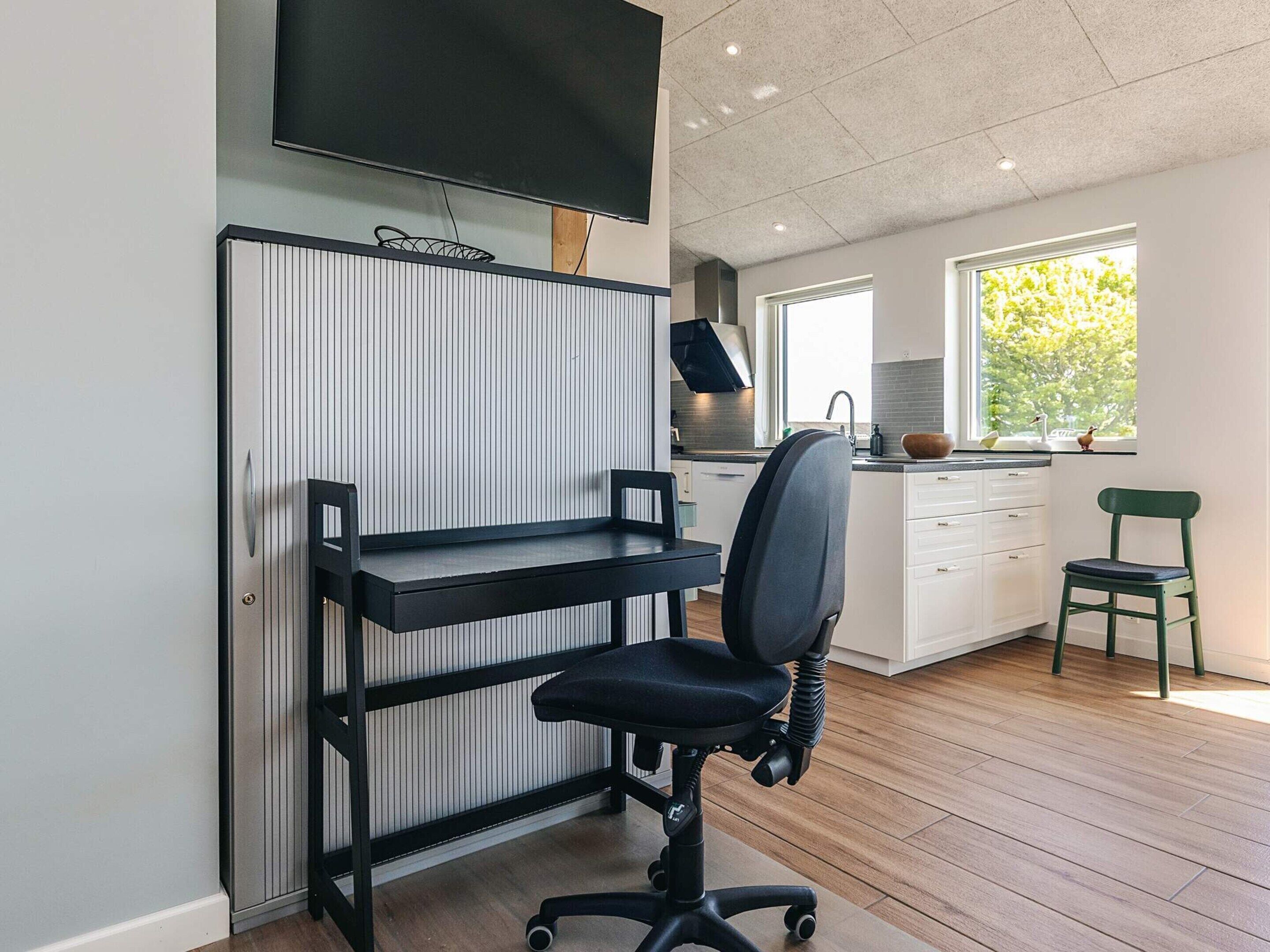 A modern kitchen with a built-in oven, a dining area with a black chair and a small table, and a large window providing natural light.