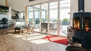 Ein großzügiger Wohnbereich mit einem großen Schiebeglastür, die auf eine Terrasse führt, einer modernen Küche und einem Kaminofen.