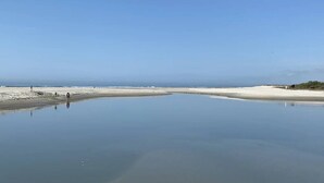 Una playa tranquila con cielo despejado, orilla arenosa y una masa de agua calma que refleja el cielo.
