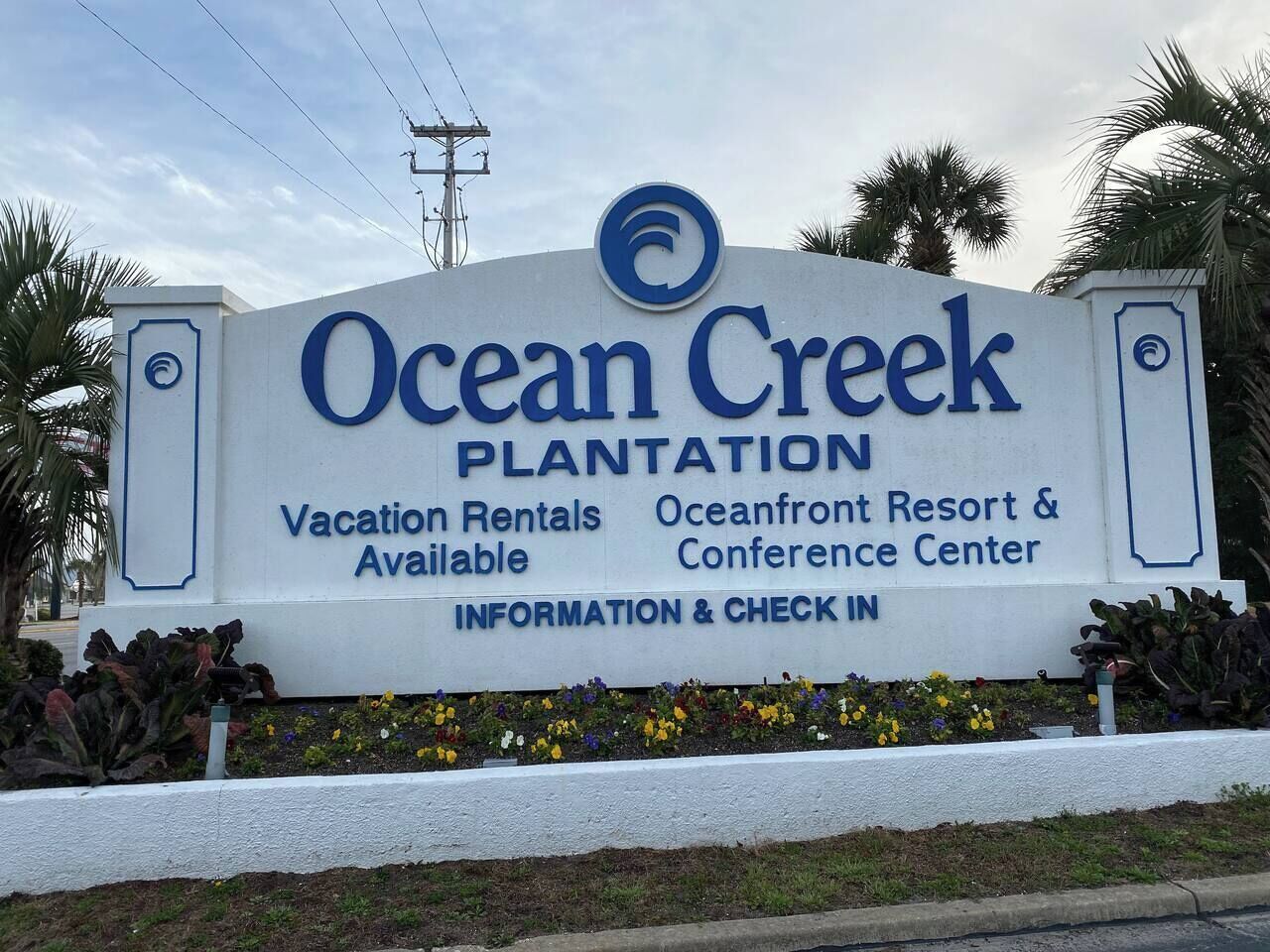 Un panneau indiquant l’emplacement d’Ocean Creek Plantation et faisant la publicité de locations de vacances, du complexe hôtelier et centre de conférences en bord de mer, ainsi que d’un espace d’information et d’enregistrement.
