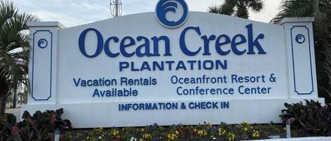 Un panneau indiquant l’emplacement d’Ocean Creek Plantation et faisant la publicité de locations de vacances, du complexe hôtelier et centre de conférences en bord de mer, ainsi que d’un espace d’information et d’enregistrement.