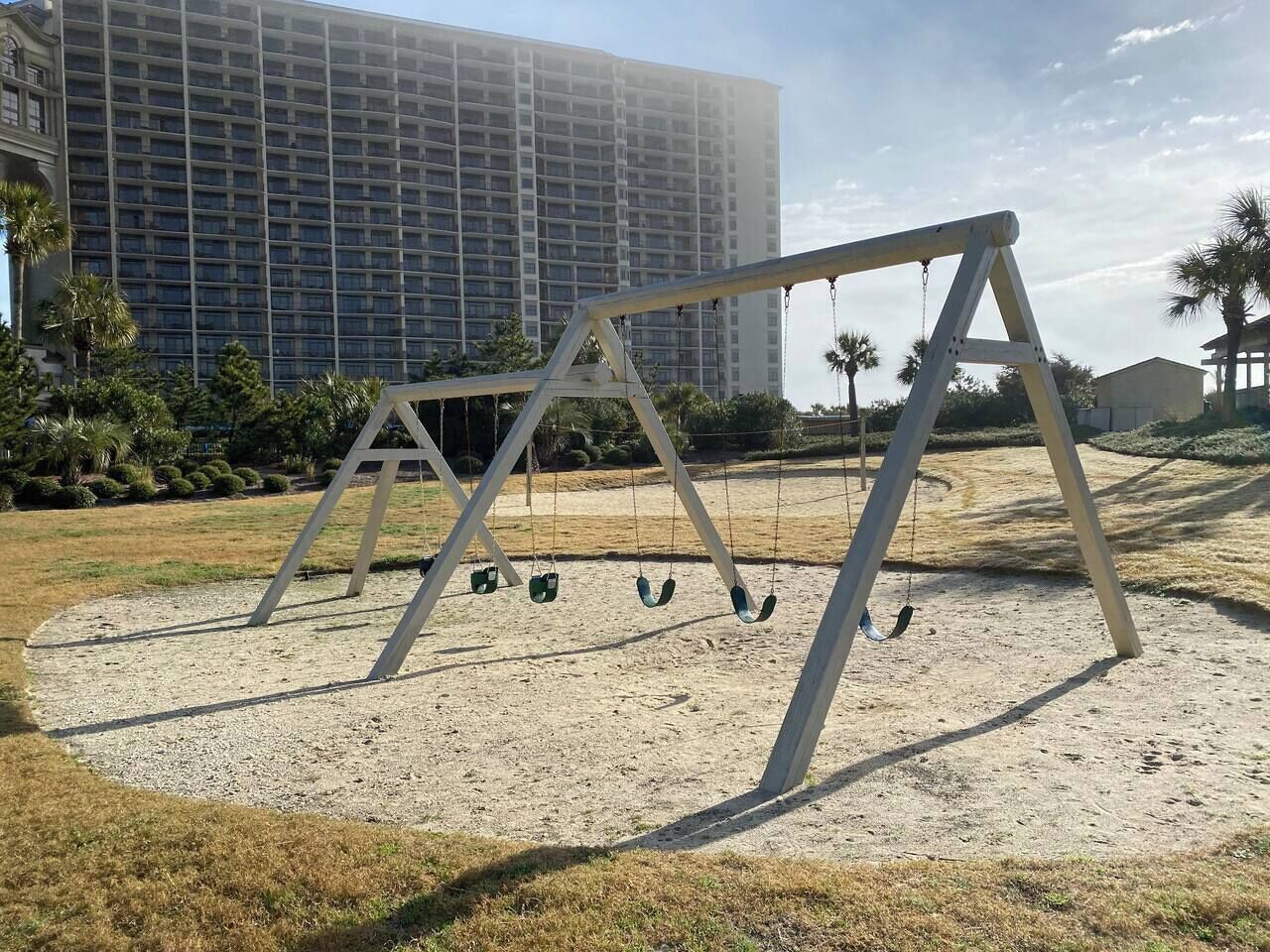 Spielplatz mit Schaukeln und einem großen Gebäude im Hintergrund.