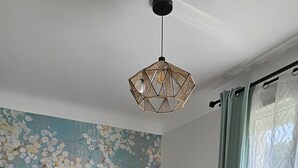 Een slaapkamer met een visgraat parketvloer, een bed met een deken van wit en donker materiaal, een wand met een bloemenmural en een hanglamp.