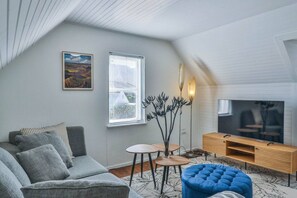 Un salon moderne avec un canapé gris, un pouf bleu, un téléviseur à écran plat et un meuble TV en bois.
