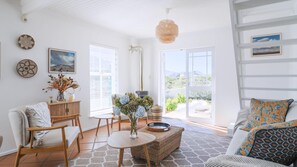 Una sala de estar luminosa con un sofá, una silla, una mesa y una lámpara colgante.